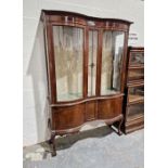 Edwardian mahogany serpentine display cabinet with glazed doors to pair of panelled cupboards below,