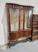 Edwardian mahogany serpentine display cabinet with glazed doors to pair of panelled cupboards below,