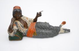 A vintage painted metal figure of a North African figure smoking in a relaxed position.