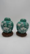 A pair of contemporary turquoise hand ground lidded ginger jars on carved pierced wooden stands. The
