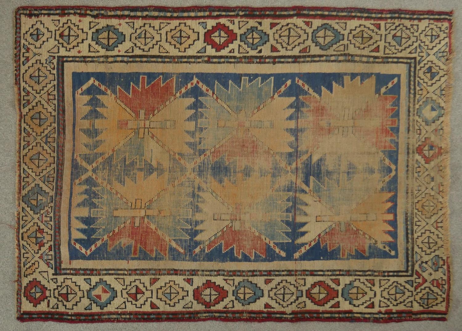 A Kazak rug with repeating star medallions on a sapphire ground within stylised multiple borders.