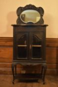 A late 19th century ebonised pier cabinet with mirrored upper section above glazed doors on carved
