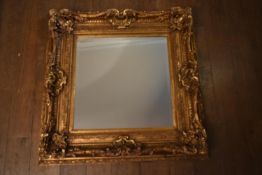 A gilt framed wall mirror in a heavy Rococo style frame, with bevelled plate. H.99 W.99cm