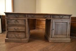 A large pine partners desk with inset leather top and an arrangement of cupboards and drawers to