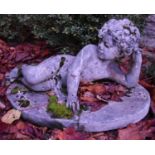 A composite garden statue of a young boy laying on his side. H.40cm