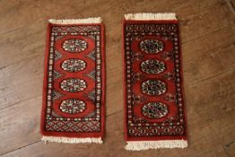 Two Pakistani Bokhara rugs on rust ground. H.70 W.30cm (2)