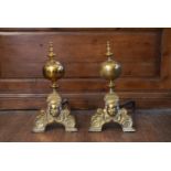 A pair of 19th century brass fire dogs with ball and finials above mask decorated base. H.51 W.