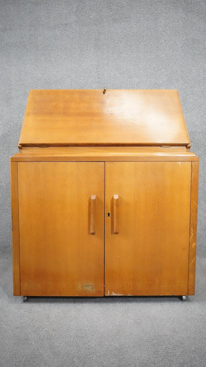 A vintage light oak bureau with fitted interior above panel doors enclosing slides. H.95cm