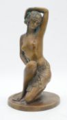 An Art Deco style brass statue of a nude kneeling woman wearing a beaded shawl and hat on circular