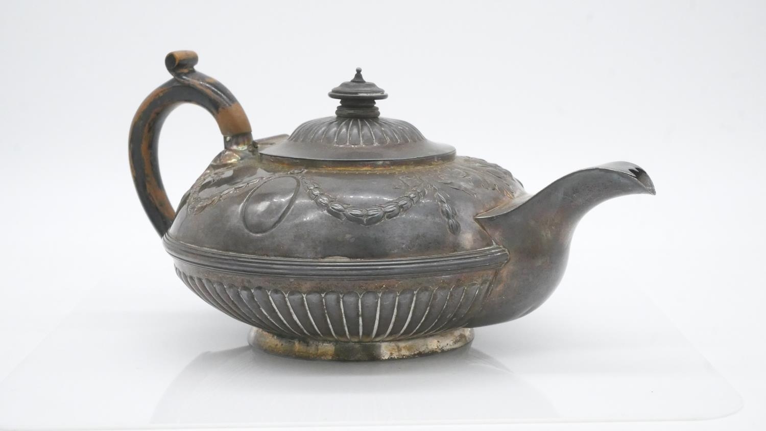 A sterling silver Georgian teapot with dragooned detailing and repousse swag and bow motifs.