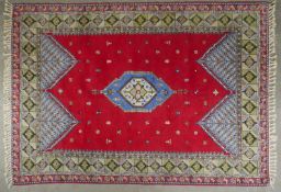 A Kazak carpet with central lozenge medallion on a burgundy ground within geometric borders. L.280