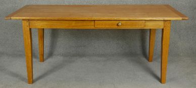 An oak planked top kitchen table with cleated ends and central frieze drawer raised on square
