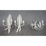 A pair of white painted twin branch wall candelabras with fern and flowerhead decoration along