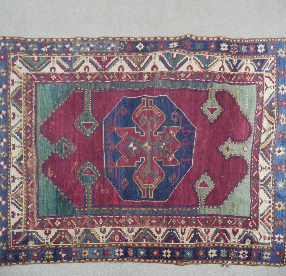 A Kazak rug with central lozenge medallion on burgundy field within jade spandrels (one signed)