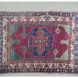 A Kazak rug with central lozenge medallion on burgundy field within jade spandrels (one signed)