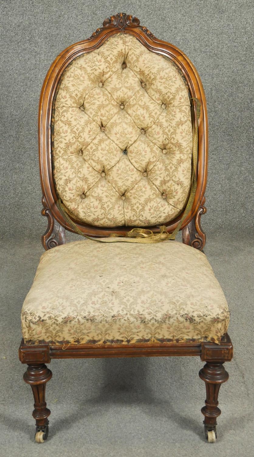 A Victorian walnut nursing chair with floral carved back rail and buttoned upholstery on tapering