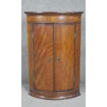 A Georgian mahogany and crossbanded bowfronted hanging corner cupboard. H93 W60 D42cm