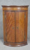 A Georgian mahogany and crossbanded bowfronted hanging corner cupboard. H93 W60 D42cm