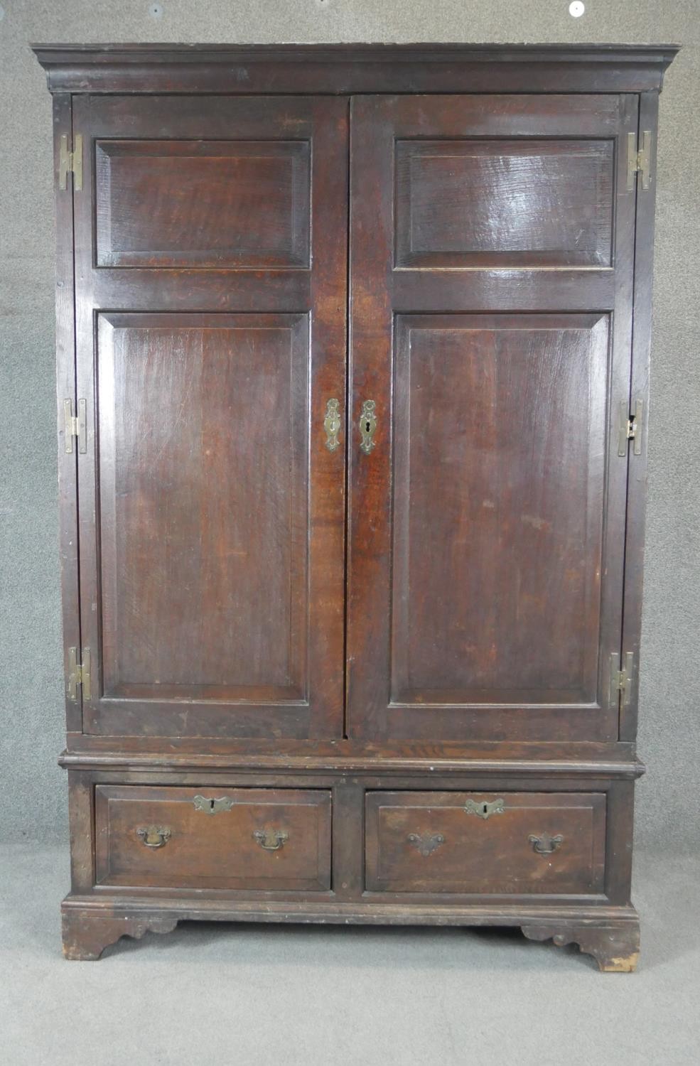 A Georgian country oak press cupboard with fielded panel doors above base doors on bracket feet.