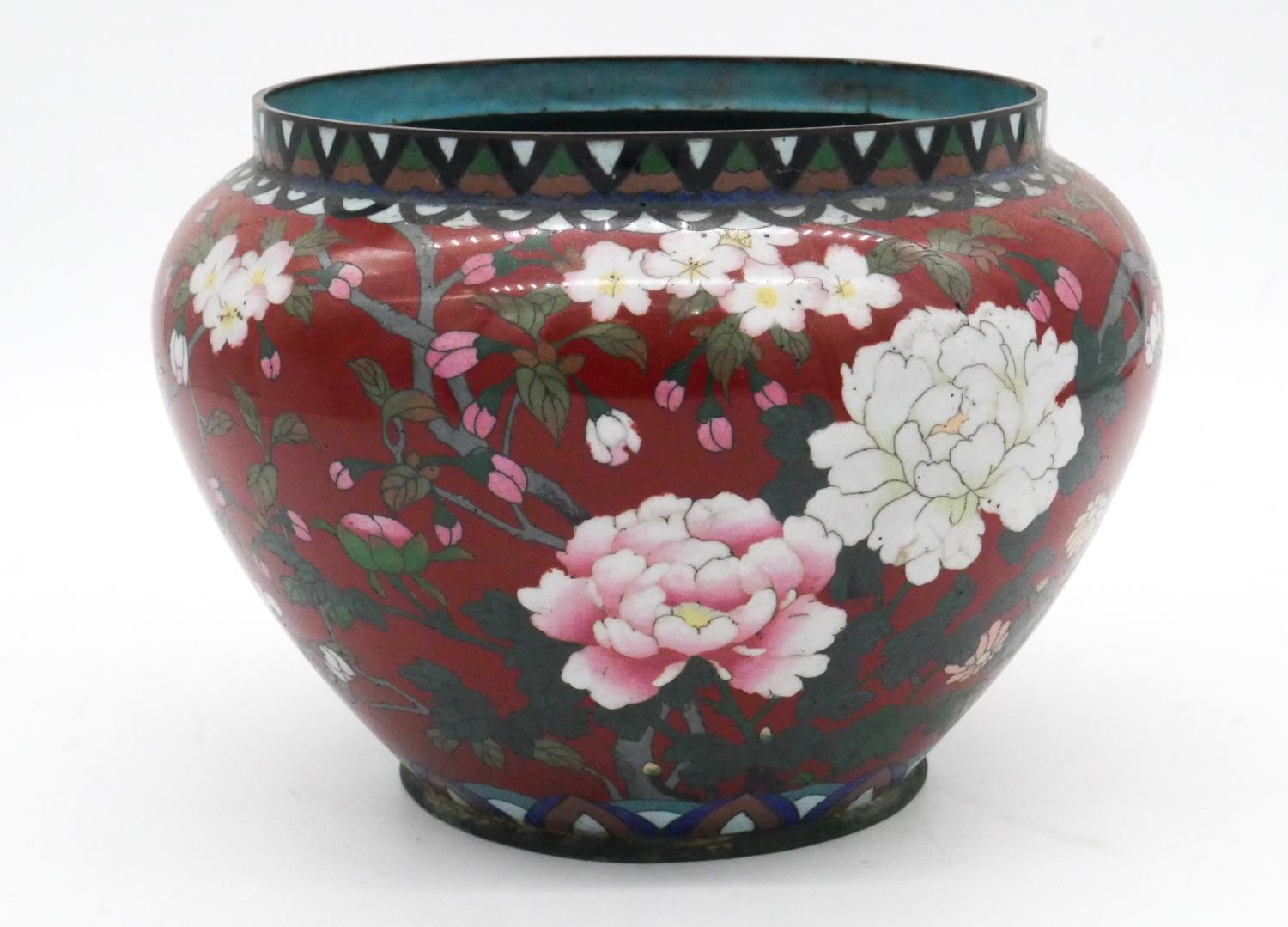 A Meji period Japanese cloisonne enamel on brass jardinere with red ground and decorated with