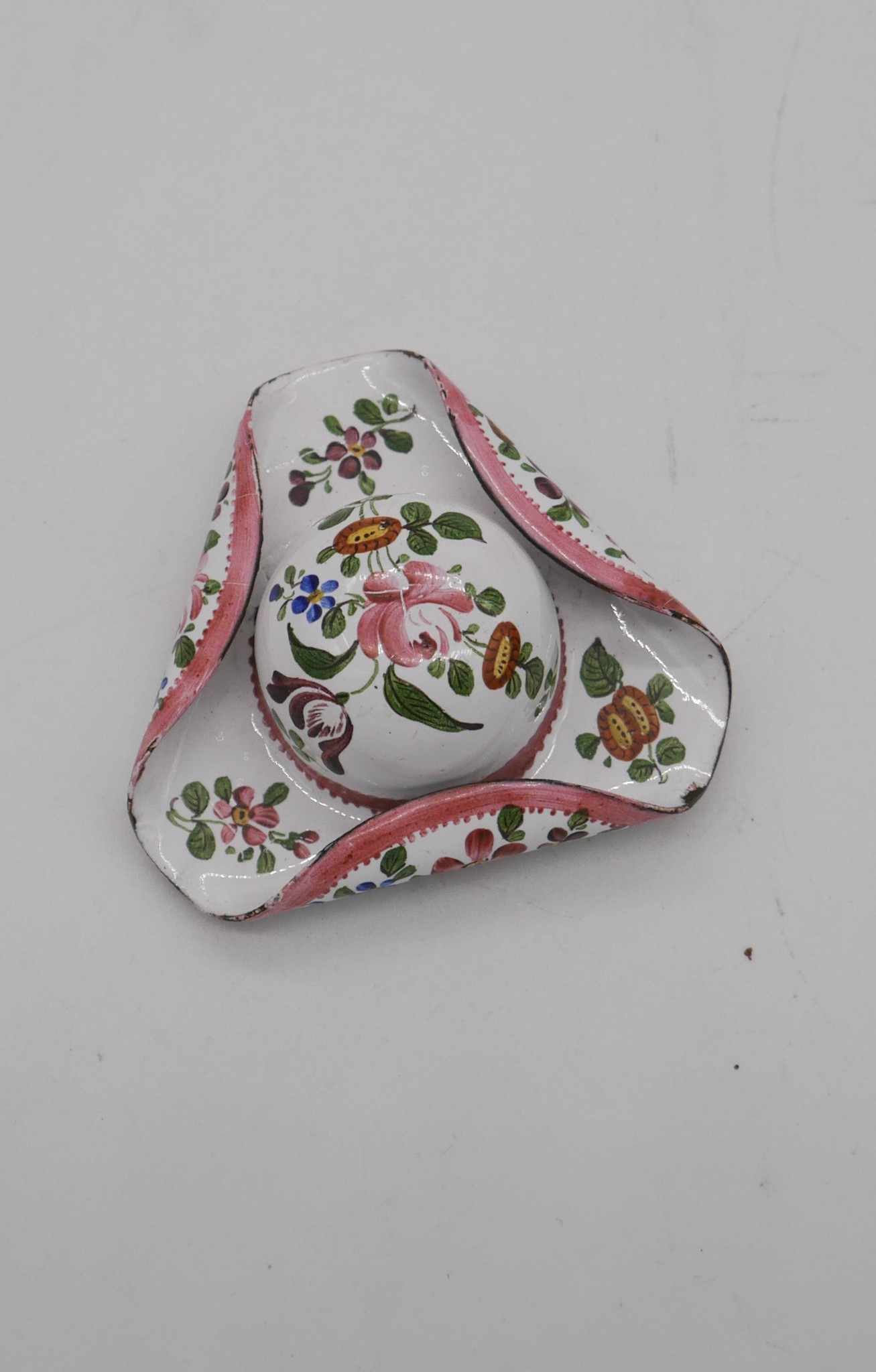 A late 19th century enamel patch box in the form of a tricorn hat, the white ground decorated with