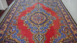 A Persian style carpet with floral central medallion on a burgundy field within foliate spandrels