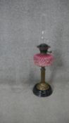 A late Victorian oil lamp, with an opaque pink glass foliate design relief well, the brass stand