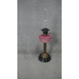 A late Victorian oil lamp, with an opaque pink glass foliate design relief well, the brass stand