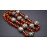 A Tibetan white metal and amber necklace. Strung with fifty seven polished amber beads, the