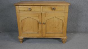 A 19th century pine side cabinet with arched panel doors on squat turned tapering supports. H.87 W.