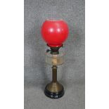 A Victorian brass oil lamp with black base and red opaque glass ball shade and glass oil well.