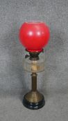 A Victorian brass oil lamp with black base and red opaque glass ball shade and glass oil well.