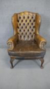 A Georgian style wing back armchair in deep buttoned leather upholstery on cabriole supports. (