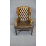 A Georgian style wing back armchair in deep buttoned leather upholstery on cabriole supports. (