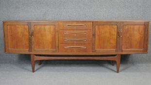 A vintage teak sideboard with central bank of drawers flanked by sliding cupboard doors on shaped