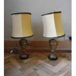 A pair of gilt brass classical design twin handled table lamps with cream shade and green fringe
