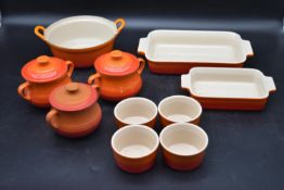 A collection of orange Le Cruset kitchenware. Including three soup bowls with lids, four ramekins,