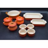 A collection of orange Le Cruset kitchenware. Including three soup bowls with lids, four ramekins,