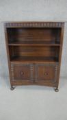 A mid century oak bookcase in the antique style with open shelves above panel doors on bun feet.