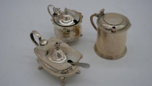 Three silver mustard pots with blue glass liners, two with spoons (one silver plate). One with a