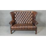 A Georgian style wingback two seater armchair in deep buttoned and studded leather upholstery on