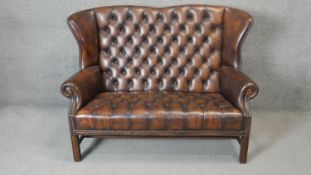 A Georgian style wingback two seater armchair in deep buttoned and studded leather upholstery on