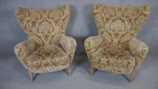 A pair of vintage wing back armchairs in cut floral moquette upholstery on splay light oak supports.