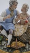 A hand painted porcelain figure group of a pair of lovers seated on a rocky outcrop with picnic