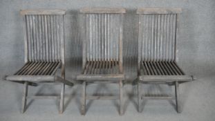 A set of three weathered teak folding slatted garden chairs.