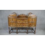 A mid century oak Jacobean style sideboard with carved cresting above lozenge panelled doors on