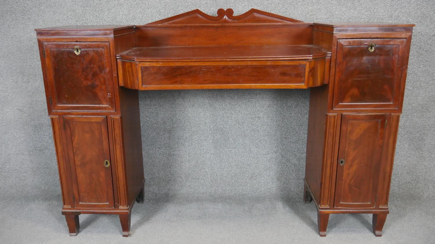 A Regency mahogany twin pedestal sideboard with flame mahogany panel doors flanked by pilasters on