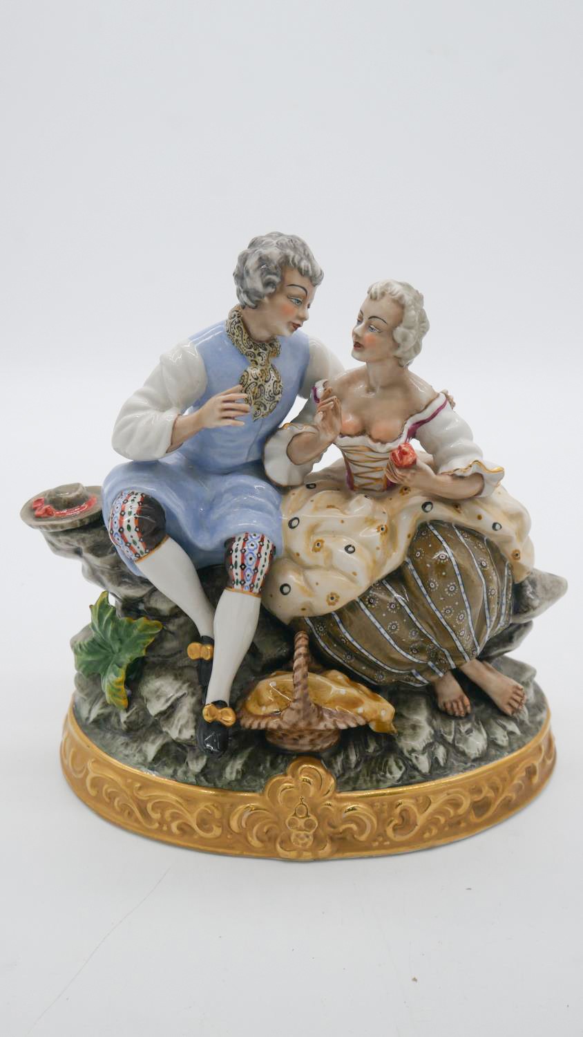 A hand painted porcelain figure group of a pair of lovers seated on a rocky outcrop with picnic