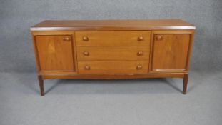 A 1970's vintage teak sideboard with central bank of drawers flanked by cupboards raised on shaped