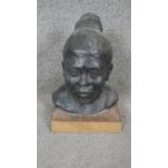 A sculpted ceramic head of a female with bun hairstyle mounted on a wooden block. H.35cm